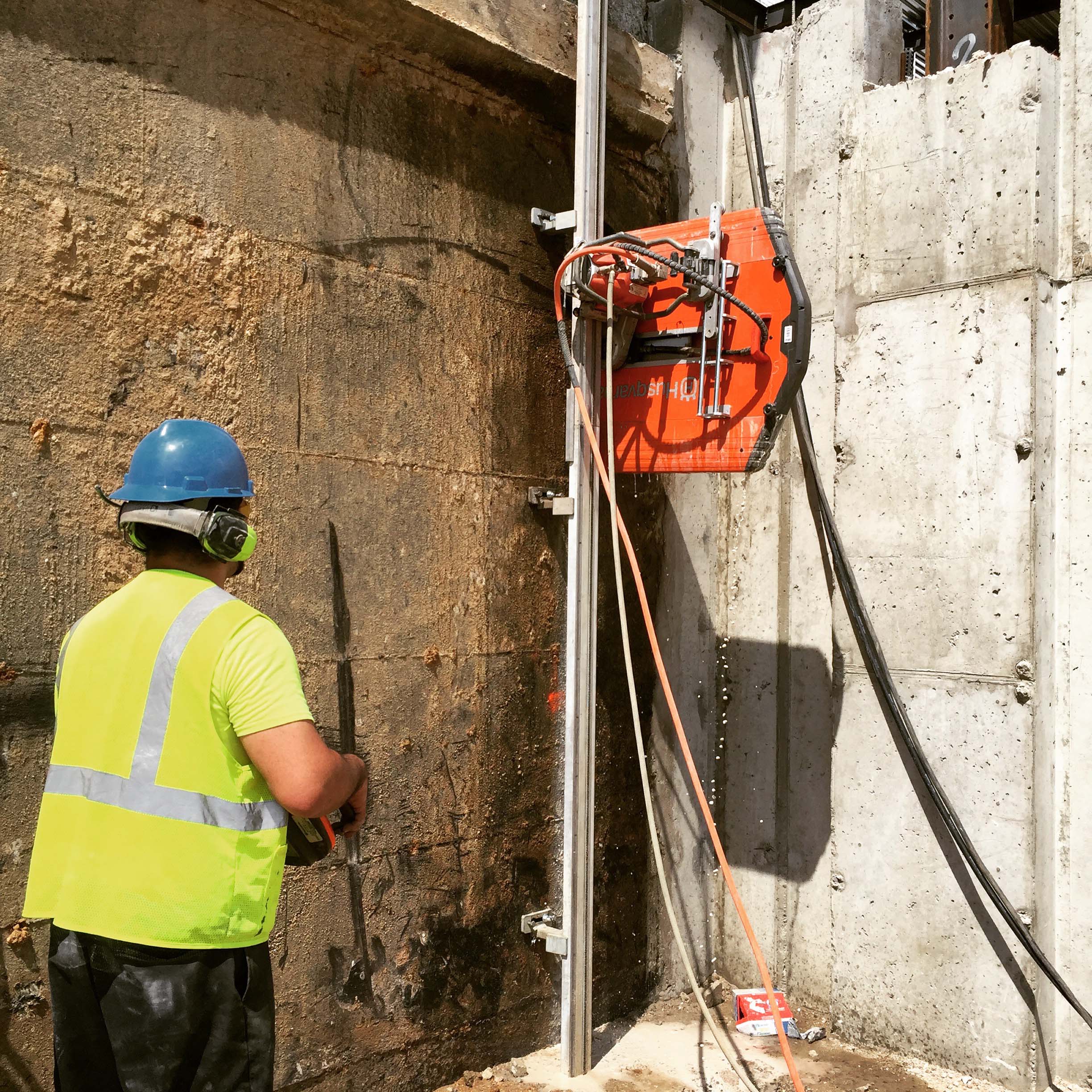 Track-mounted wall saw cutting through reinforced concrete wall at construction site